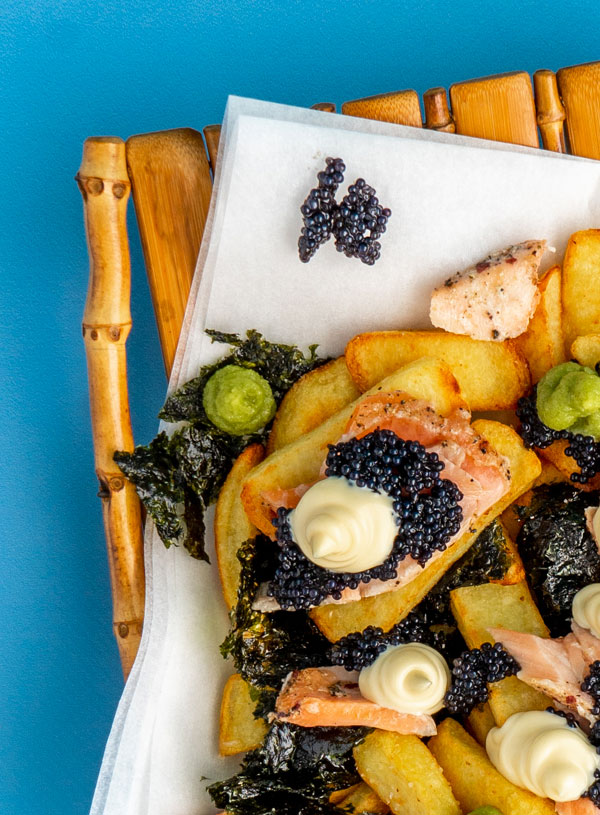 A bamboo plate filled with fries, flakes of smoked salmon, tufts of wasabi and mayo and dollops of caviar