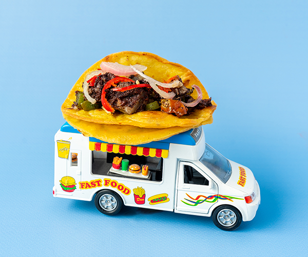 A brightly colored toy foodtruck with a taco filled with black pudding, green peppers, red chilies and pickled shallots atop a blue backdrop.