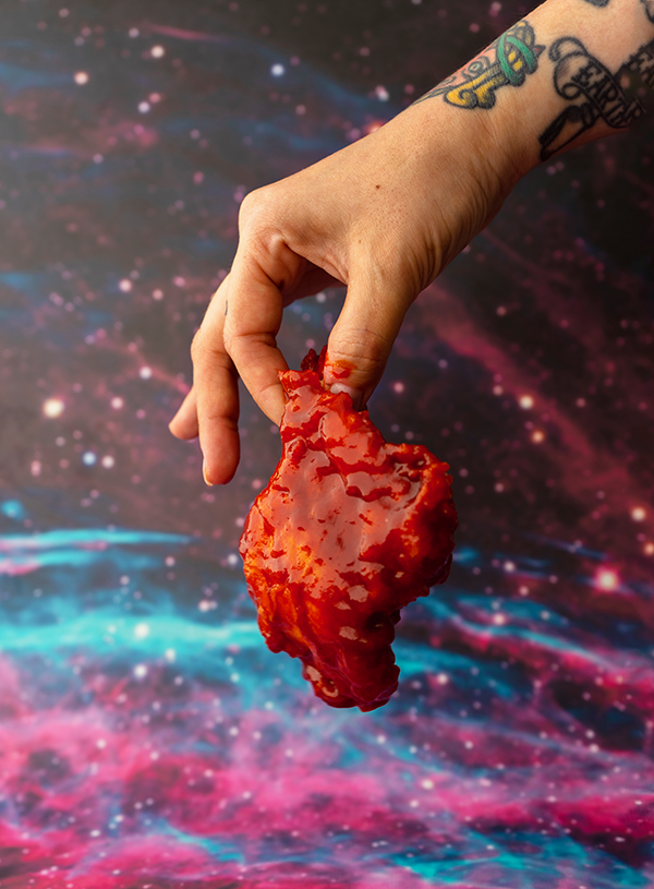 A hand holding a piece of Korean fried chicken in front of a space backdrop