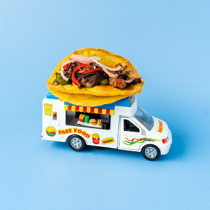 A miniature foodtruck with a Boudin Noir taco on top, in front of a blue backdrop