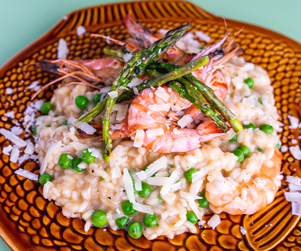 A brown fish shaped plate with a portion of seafood risotto with peas and green asparagus on top