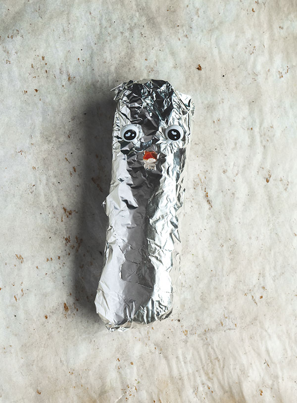 A tin foil wrapped veggie sweet potato burrito with a face on it