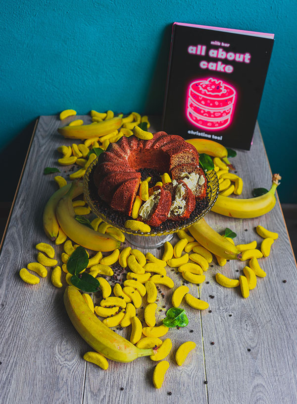 A banana curry cake surrounded by Haribo candy bananas and the book All About Cake by Christina Tosi