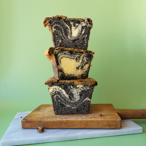 Slices of black sesame swirl pound cake stacked on top of each other on marble and wooden cutting boards with a light green background