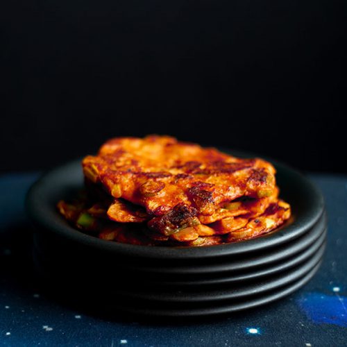 A stack of easy vegan kimchi pancakes on a stack of small black plates floating in space