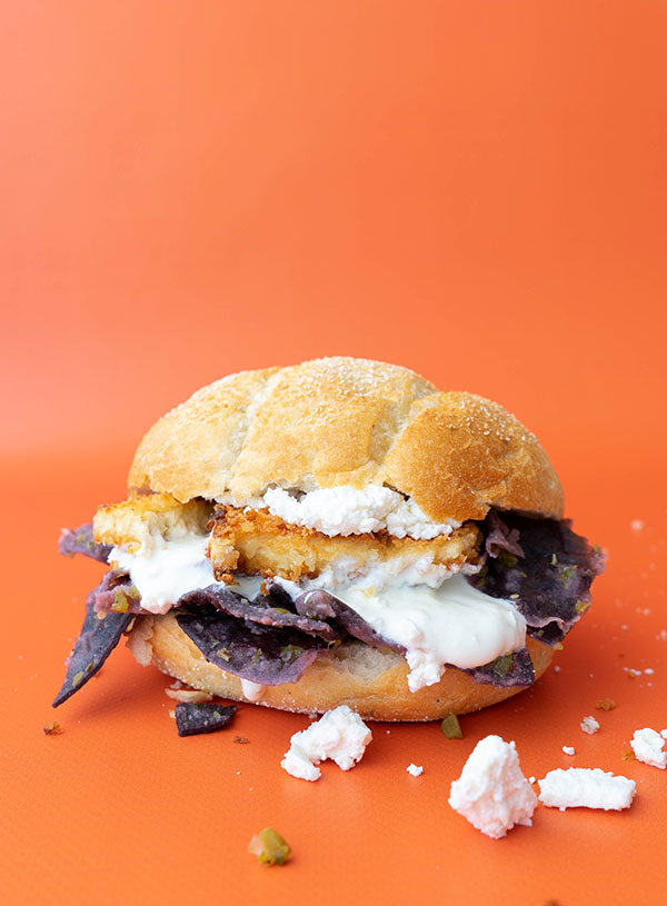 A tortas de chilaquiles (chilaquiles bread roll) with chilaquiles made with black totopos, sour cream, tofu schnitzel and feta cheese.