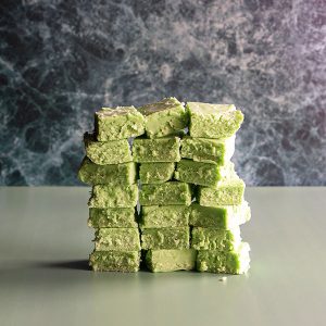 A wall made with green pandan fudge pieces in stacks of seven and rows of three, on a green marble and plain green backdrop.